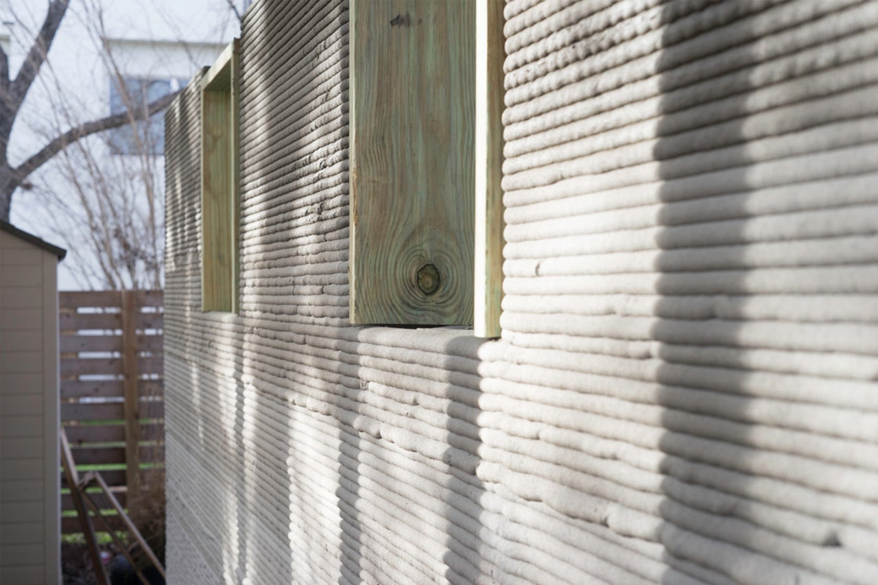 Nahaufnahme einer Hauswand aus 3D-gedrucktem Beton mit Holzrahmen für Fensteröffnungen