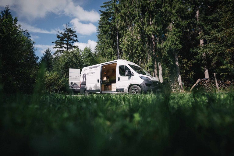 Ein weißer Lieferwagen mit der Aufschrift BUILDIFY parkt im Wald, die Tür steht offen.