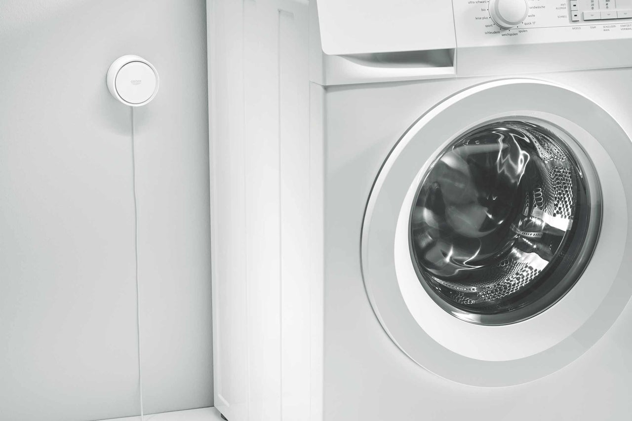 Weiße Waschmaschine mit Grohe Sense Guard Wassersensor an der Wand