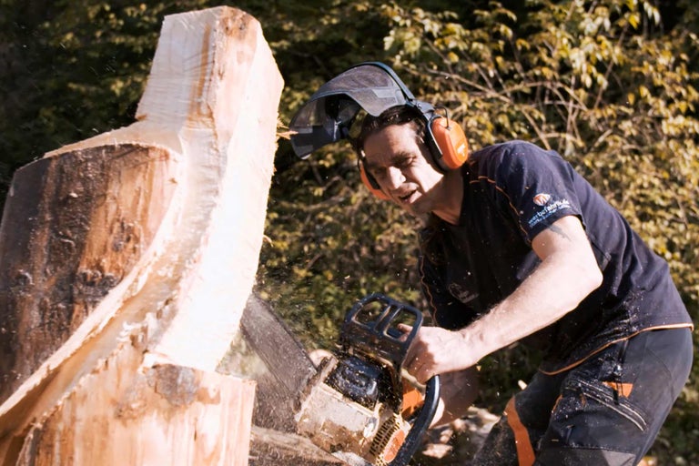 Mann mit Kettensäge beim Holzbearbeiten mit Sicherheitsausrüstung