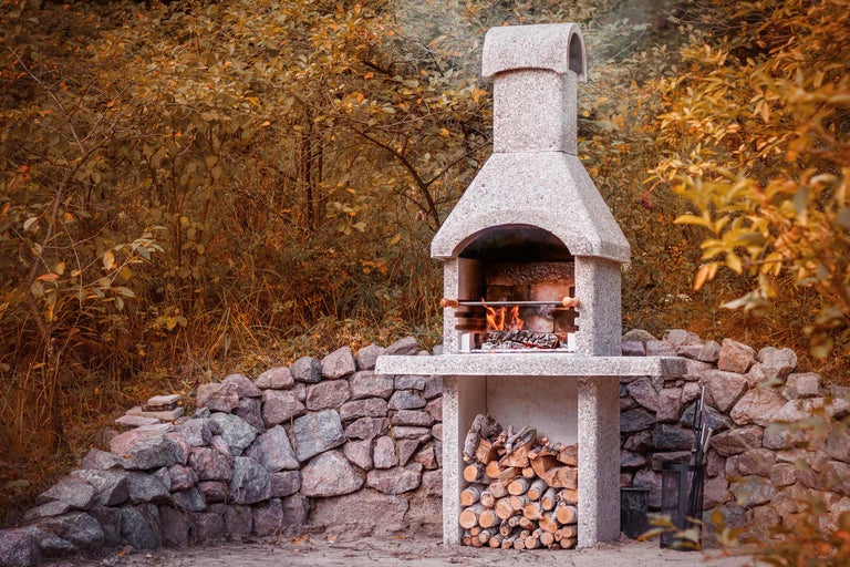 Gemauerter Gartengrill mit Holzstapel und Steinmauer im Außenbereich.
