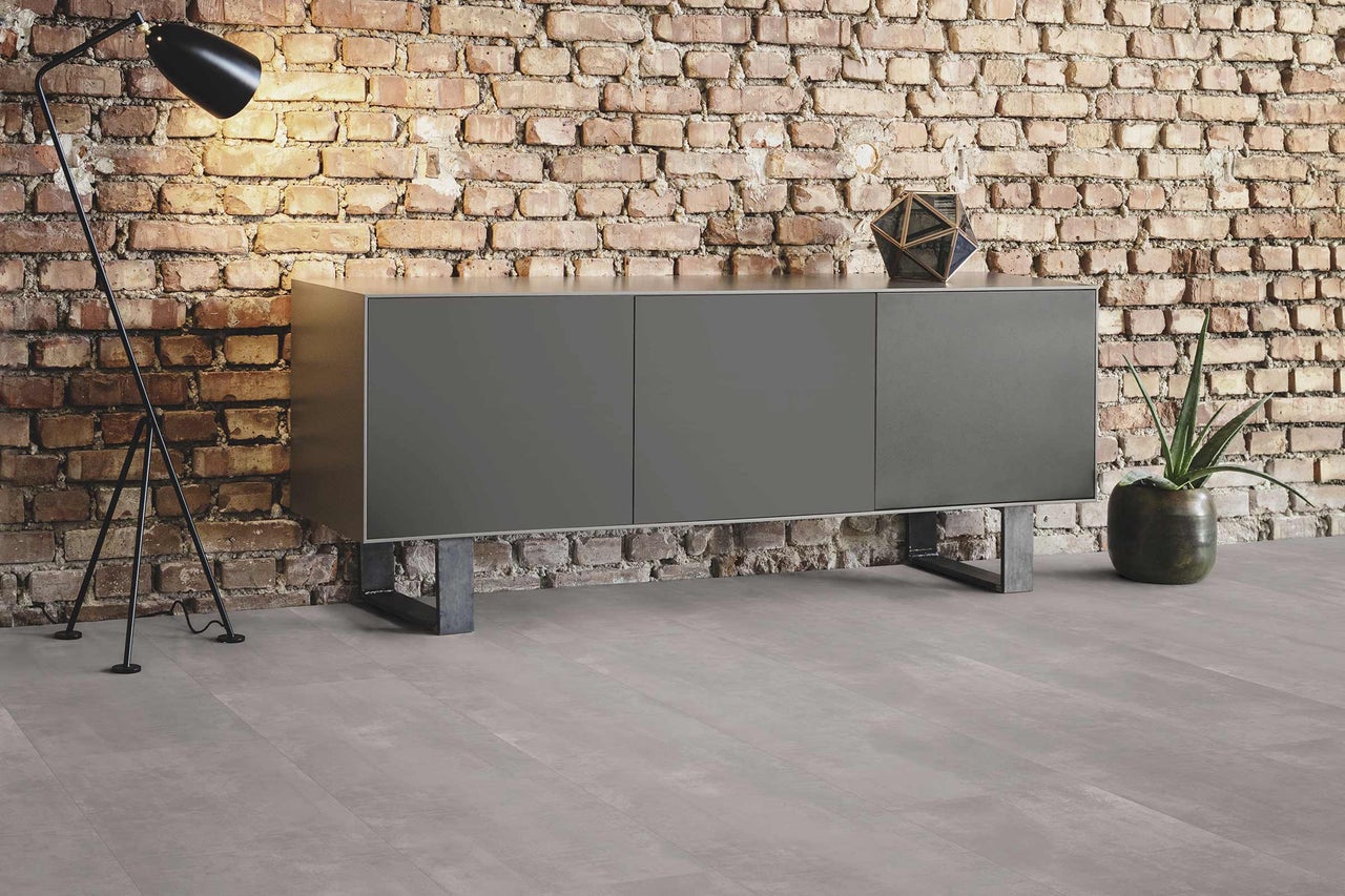 Modernes Wohnzimmer mit Sideboard, Stehlampe und Zimmerpflanze vor Ziegelwand