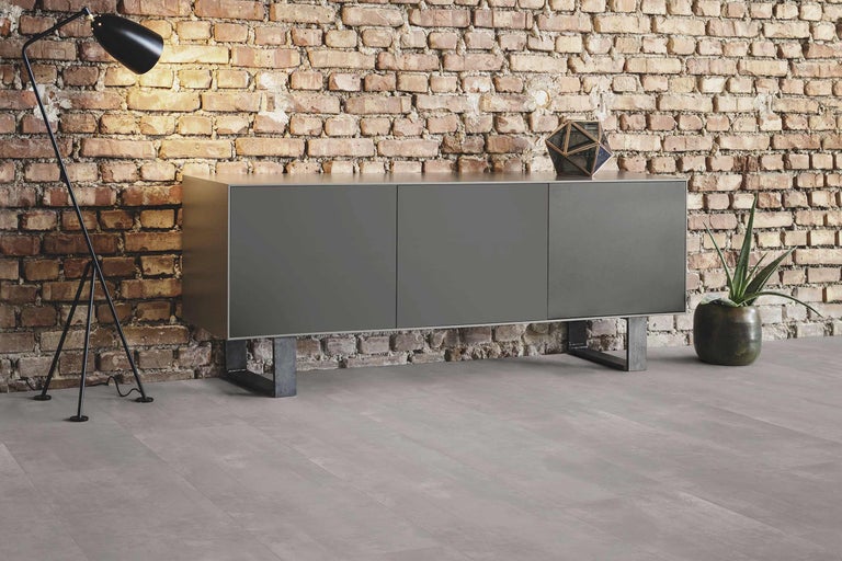 Modernes Wohnzimmer mit Sideboard, Stehlampe und Zimmerpflanze vor Ziegelwand