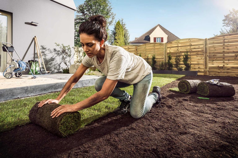 Frau verlegt Rollrasen im Garten.