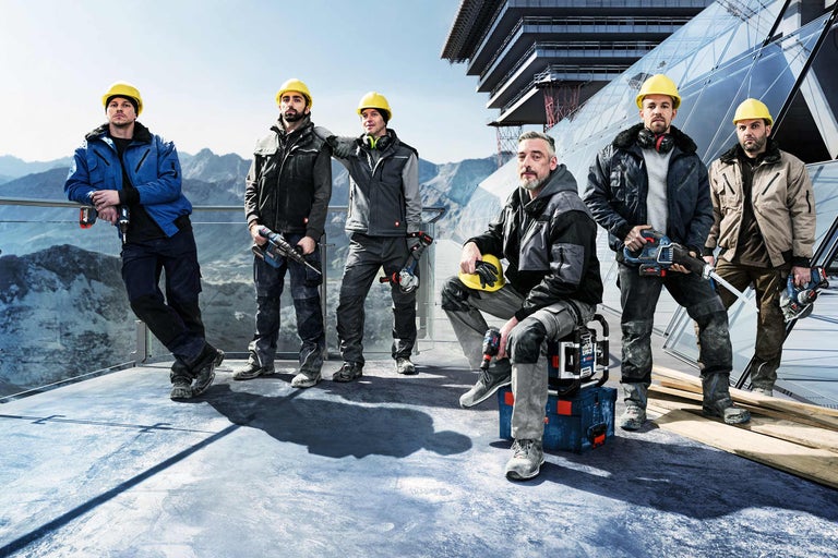Gruppe von Bauarbeitern mit Werkzeugen und Schutzkleidung vor einem Bauprojekt