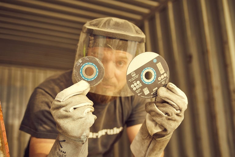 Mann mit Gesichtsschutz und Arbeitshandschuhen hält zwei Trennscheiben in der Hand.