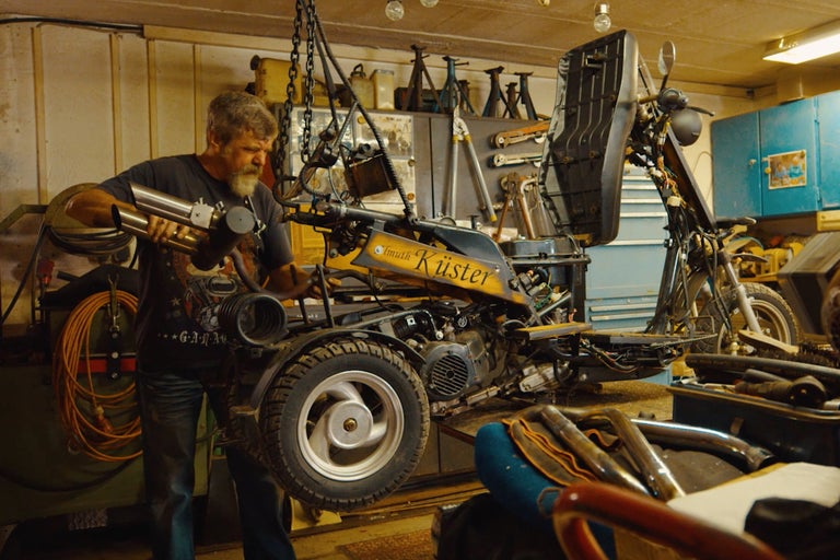 Werkstatt-Szene mit einer Person, die an einem Motorroller arbeitet, der mit einer Kette aufgehängt ist