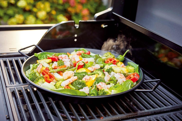 Gemüse und Garnelen in einer Grillpfanne auf einem Grill