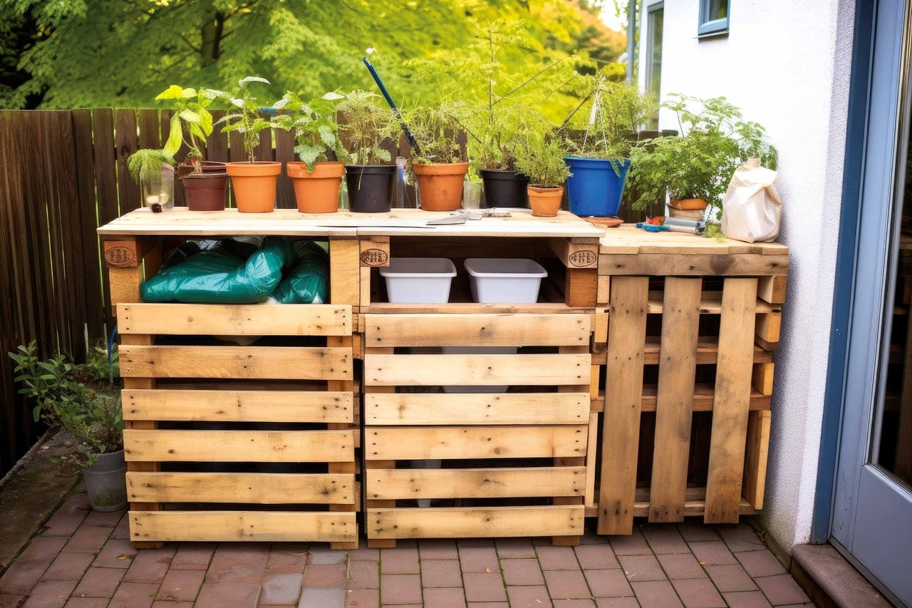 Gartenszene mit einem Regal aus Holzpaletten, bepflanzt mit verschiedenen Topfpflanzen
