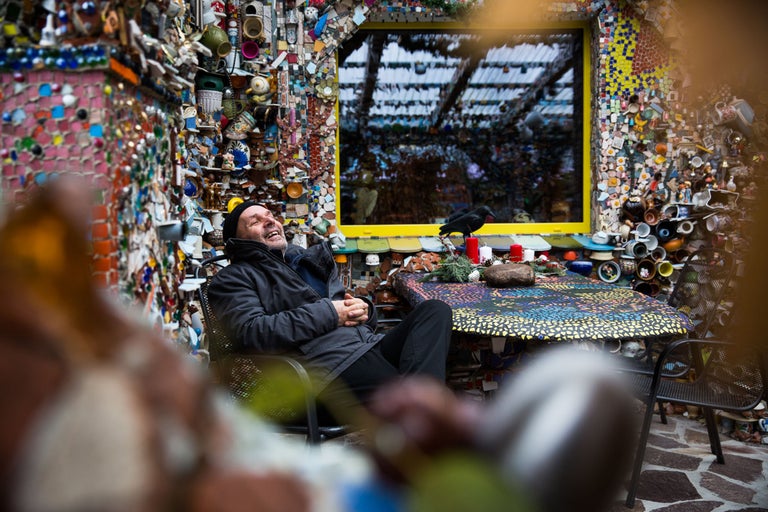 Mann sitzt an einem Tisch in einem Gartenhaus, das mit Mosaiken und Keramik verziert ist