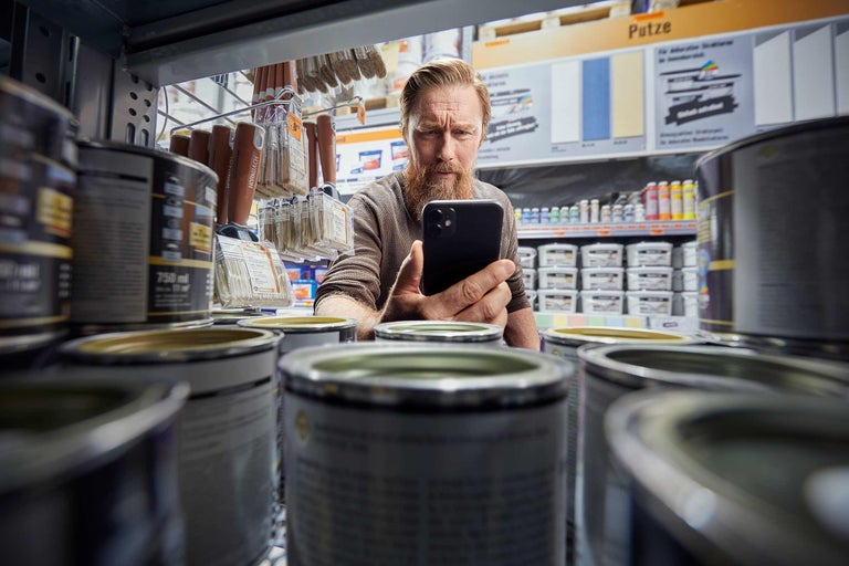 Mann fotografiert Farbeimer im Hornbach Markt mit einem Smartphone.