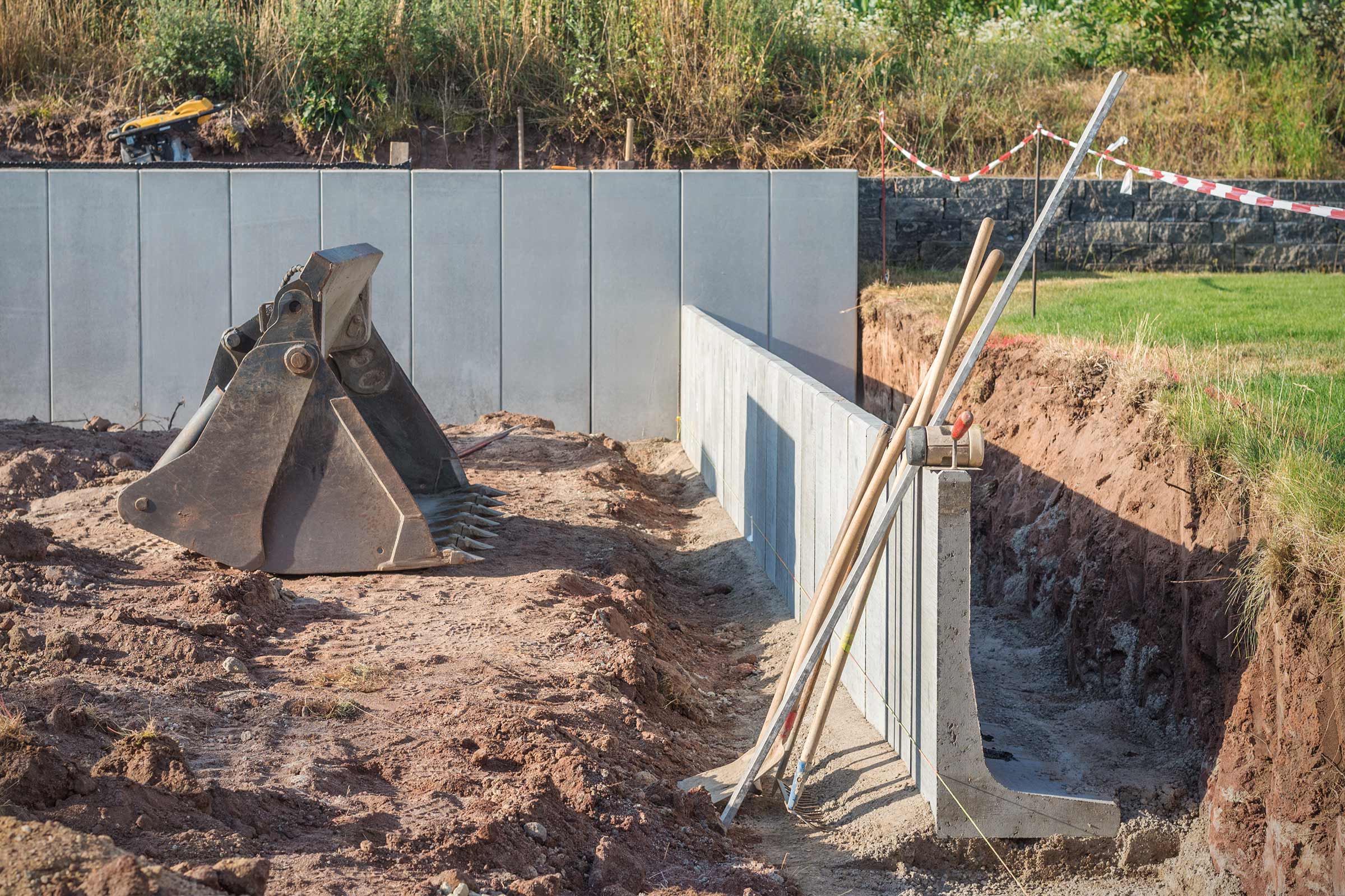 Bauarbeiten mit Betonmauer, Baggerschaufel und Werkzeugen in einer Baugrube.