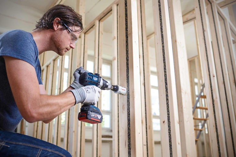 Ein Mann bohrt mit einer Bohrmaschine ein Loch in eine Holzwand.