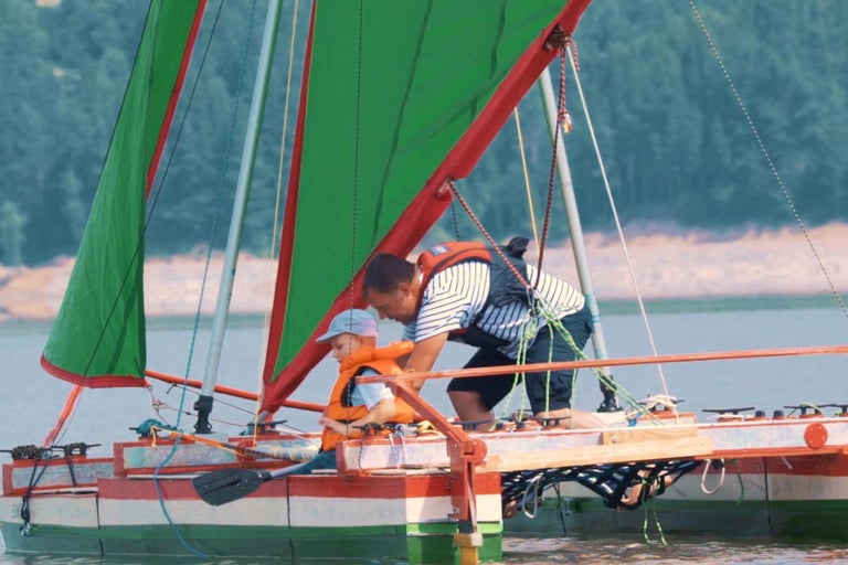 Mann und Kind mit Schwimmwesten auf Segelboot.
