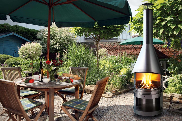 Szene im Garten mit einem Esstisch unter einem Sonnenschirm und einem Kaminofen