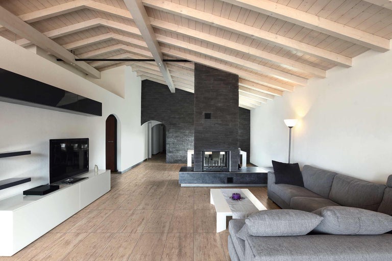 Wohnzimmer mit Kamin, grauer Couch und Holzbalkendecke