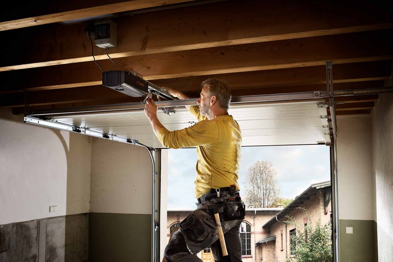 Ein Mann montiert einen Garagentorantrieb in einer Garage.
