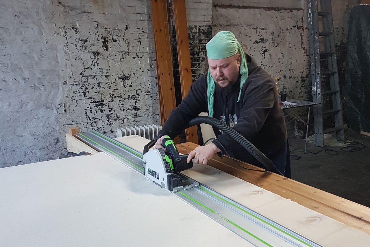 Handwerker beim Zuschneiden einer Platte mit einer Handkreissäge und Führungsschiene in einer Werkstatt