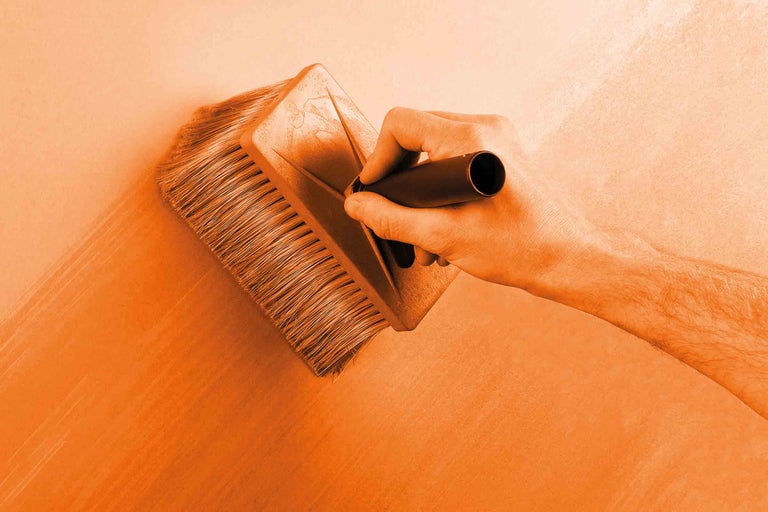 Eine Person streicht mit einem Flächenstreicher eine Wand.