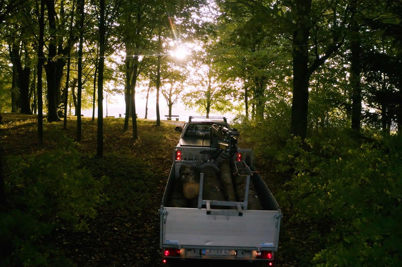 Ein Pickup-Truck mit Baumstämmen fährt durch einen Wald.