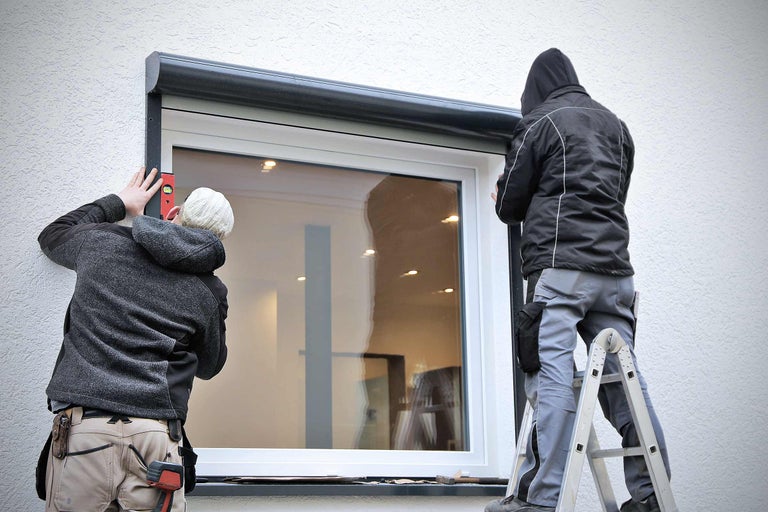 Zwei Monteure installieren einen Rollladen an einem Fenster.