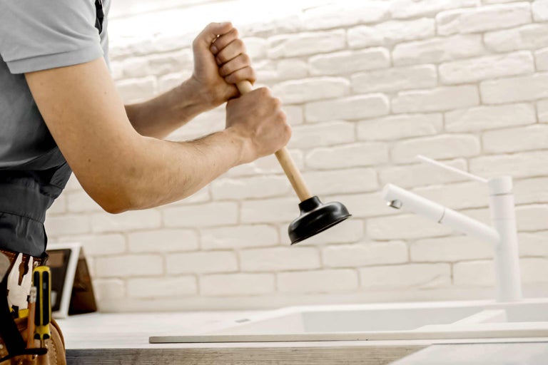 Handwerker benutzt einen Pömpel an einem Waschbecken.