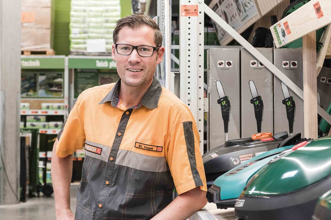 Ein Hornbach Mitarbeiter steht im Markt neben Rasenmähern und Kettensägen