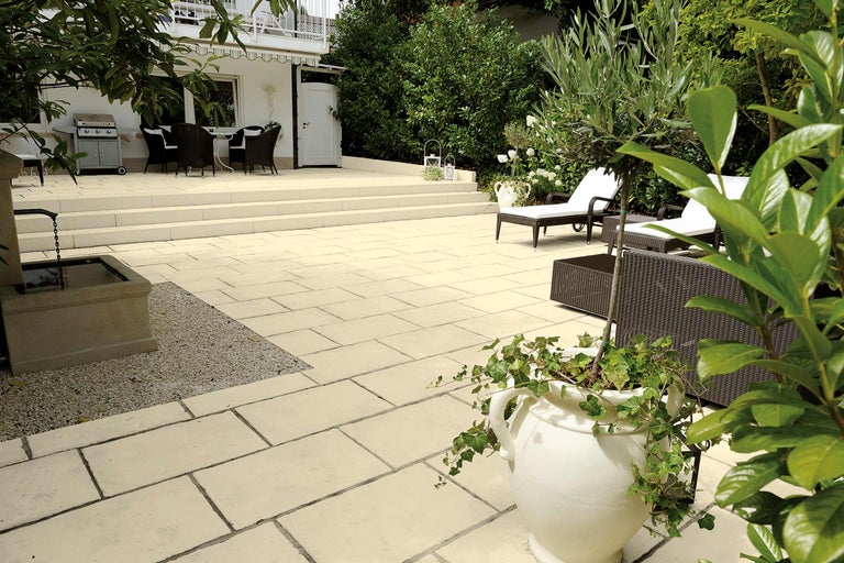 Terrasse mit Steinplatten, Grill, Gartenmöbeln und Pflanzen.