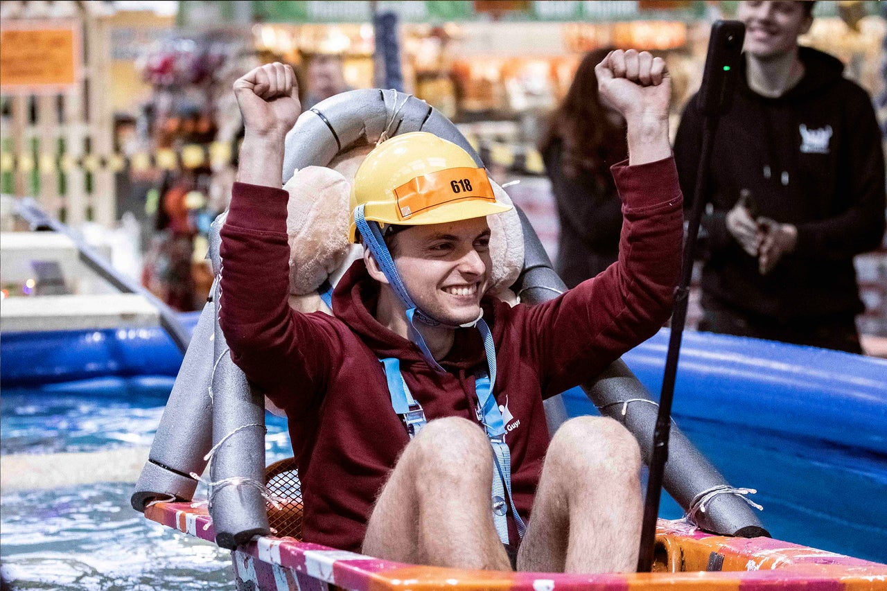 Mann mit Bauhelm und Startnummer jubelt in einem selbstgebauten Boot auf dem Wasser