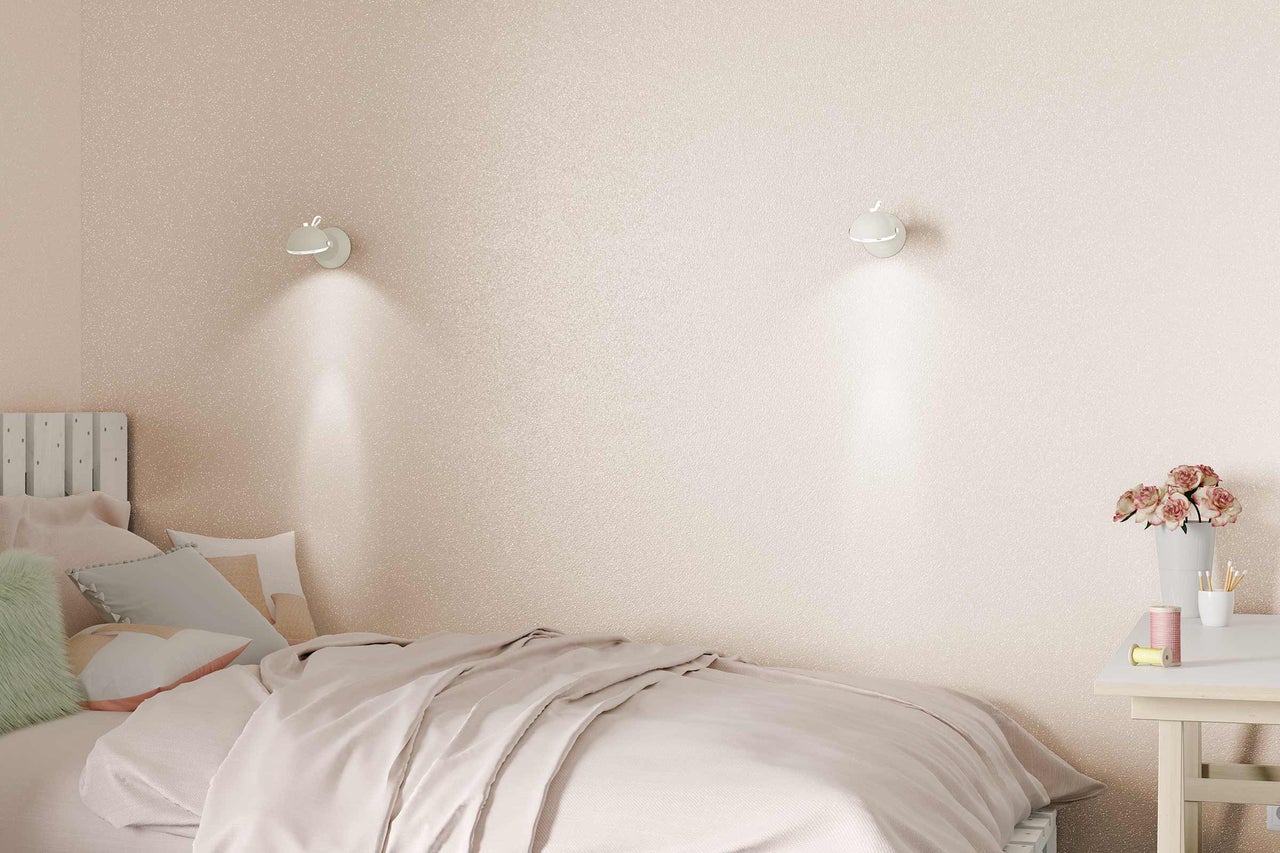 Schlafzimmer mit Bett, Nachttisch und Wandleuchten vor glitzernder Tapete