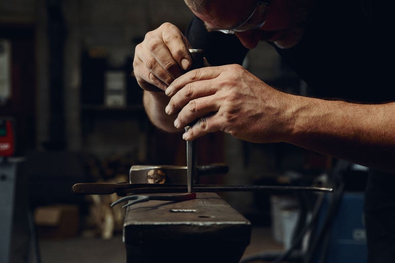 Schmied bearbeitet glühendes Metall mit einem Meißel auf einem Amboss