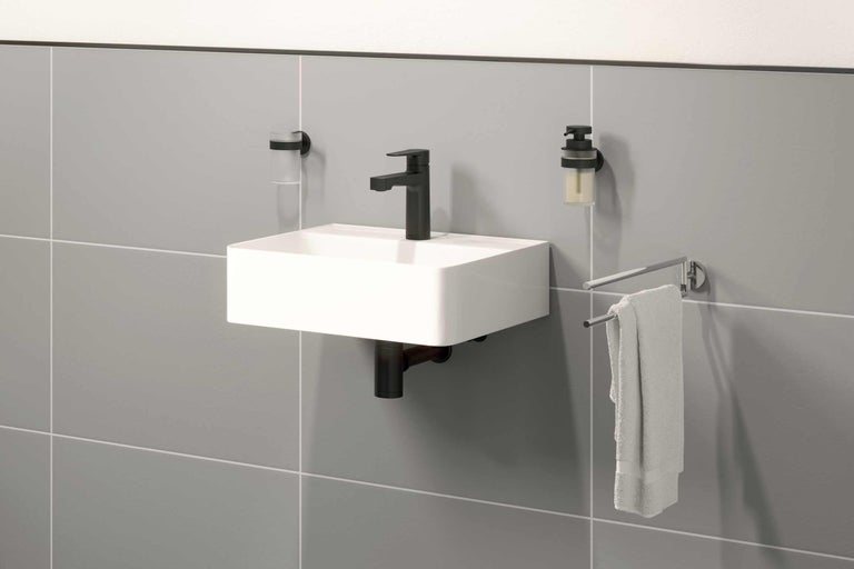 Waschtisch mit Armatur, Seifenspender, Zahnputzbecher und Handtuchhalter an grauer Wand