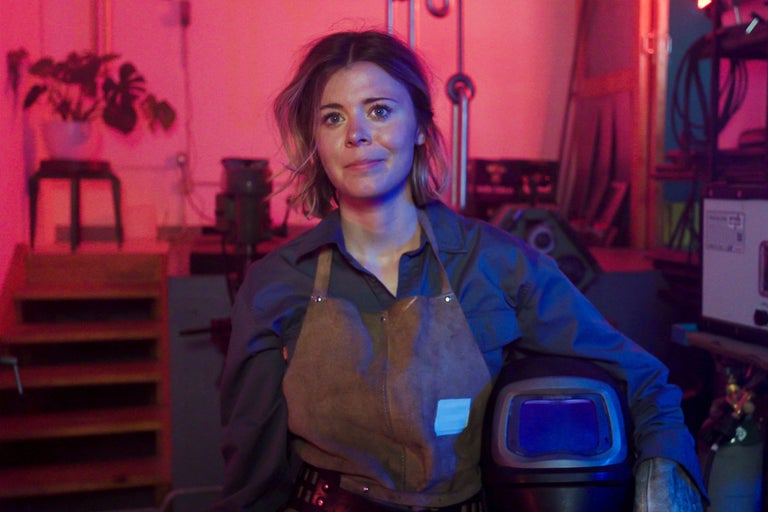 Frau mit Schweißerhelm, Lederschürze und Handschuhen in der Werkstatt