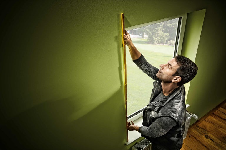 Mann misst Fensterrahmen mit Zollstock