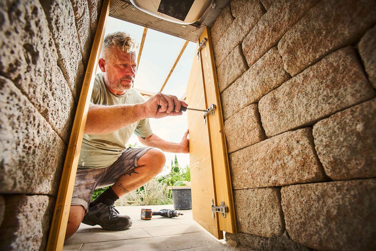 Mann montiert eine Holztür in einer Mauer mit einem Schraubenzieher