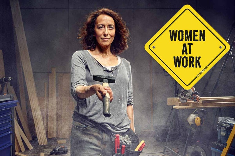 Frau mit Hammer in Werkstatt mit Werkzeugen und Women at Work Schild