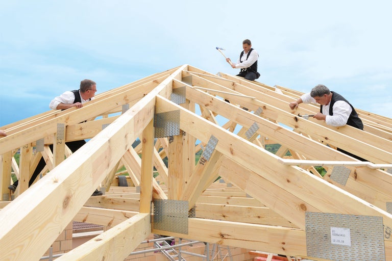 Zimmerleute bei der Montage eines Holzrahmendachs mit Metallverbindern.