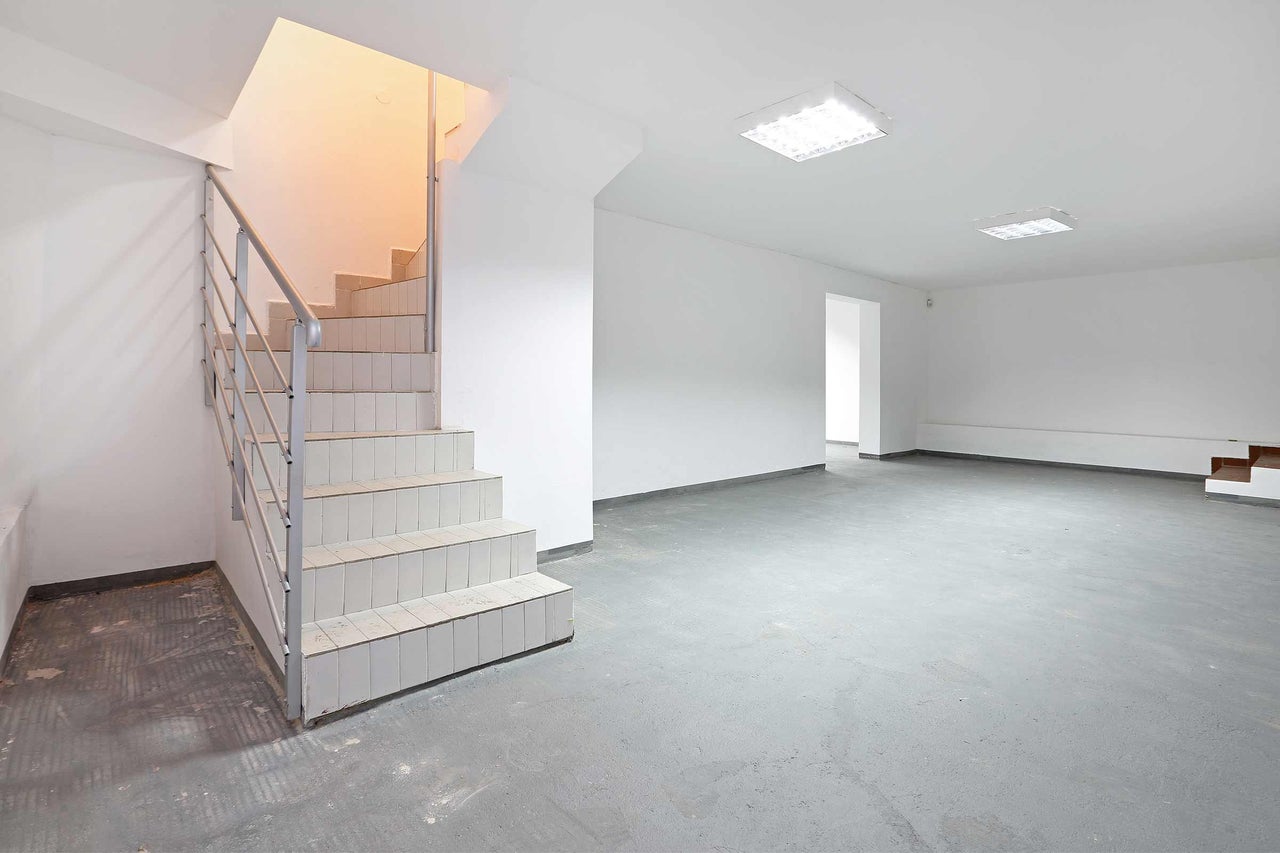 Heller Kellerraum mit Treppe, grauer Betonboden und Deckenleuchten