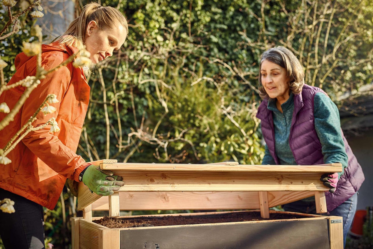 Zwei Frauen montieren ein Hochbeet im Garten.