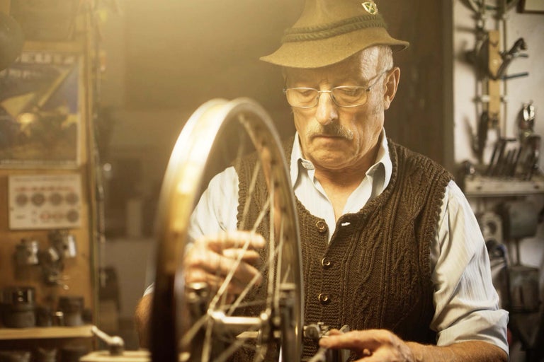 Ein Mann mit Hut repariert ein Fahrrad in einer Werkstatt.