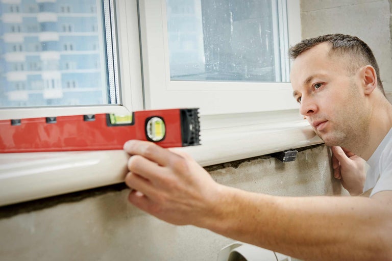 Mann benutzt Wasserwaage an Fensterbank