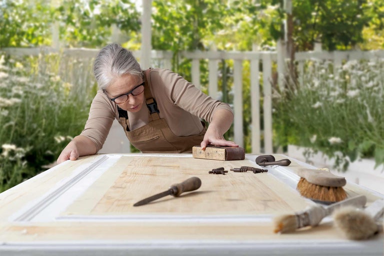 Frau schleift Holztür mit Schleifpapier und Werkzeugen