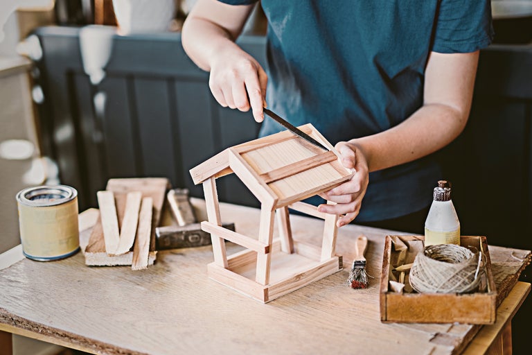 Eine Person feilt an einem hölzernen Vogelhaus auf einem Tisch mit Werkzeugen.