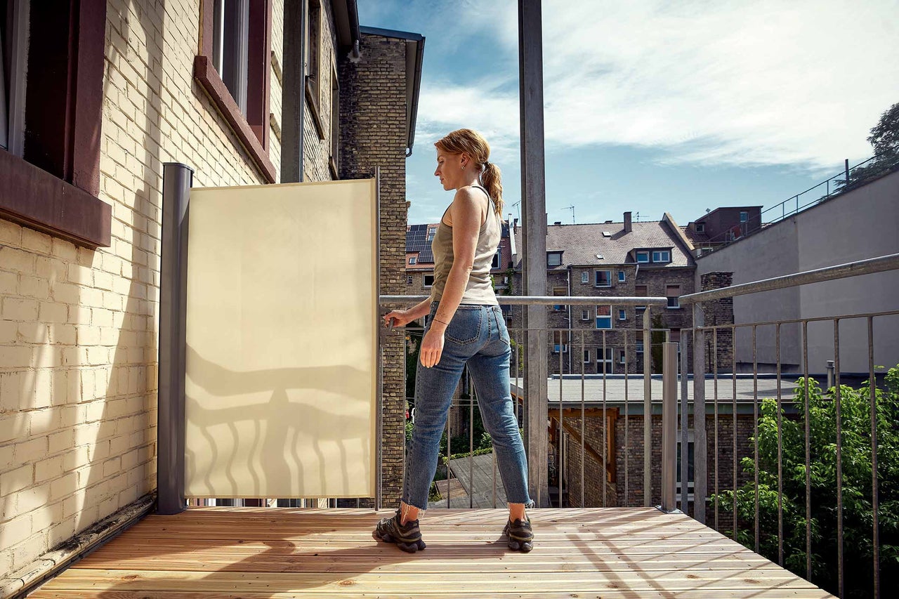 Frau bedient Sichtschutzrollo auf dem Balkon