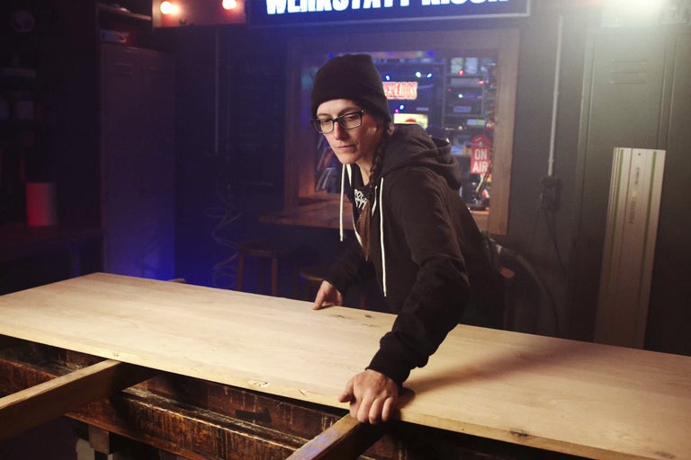 Eine Person arbeitet an einer Holzplatte in einer Werkstatt.