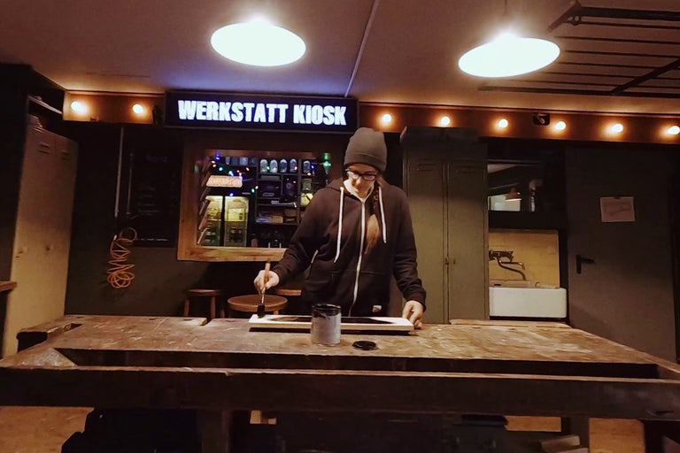 Frau streicht Holzbrett in einer Werkstatt.