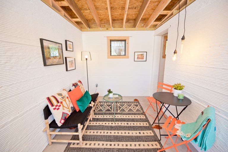 Innenraum mit Sofa, Tisch, Stühlen und Teppich in einem Haus mit dreidimensional gedruckten Wänden.