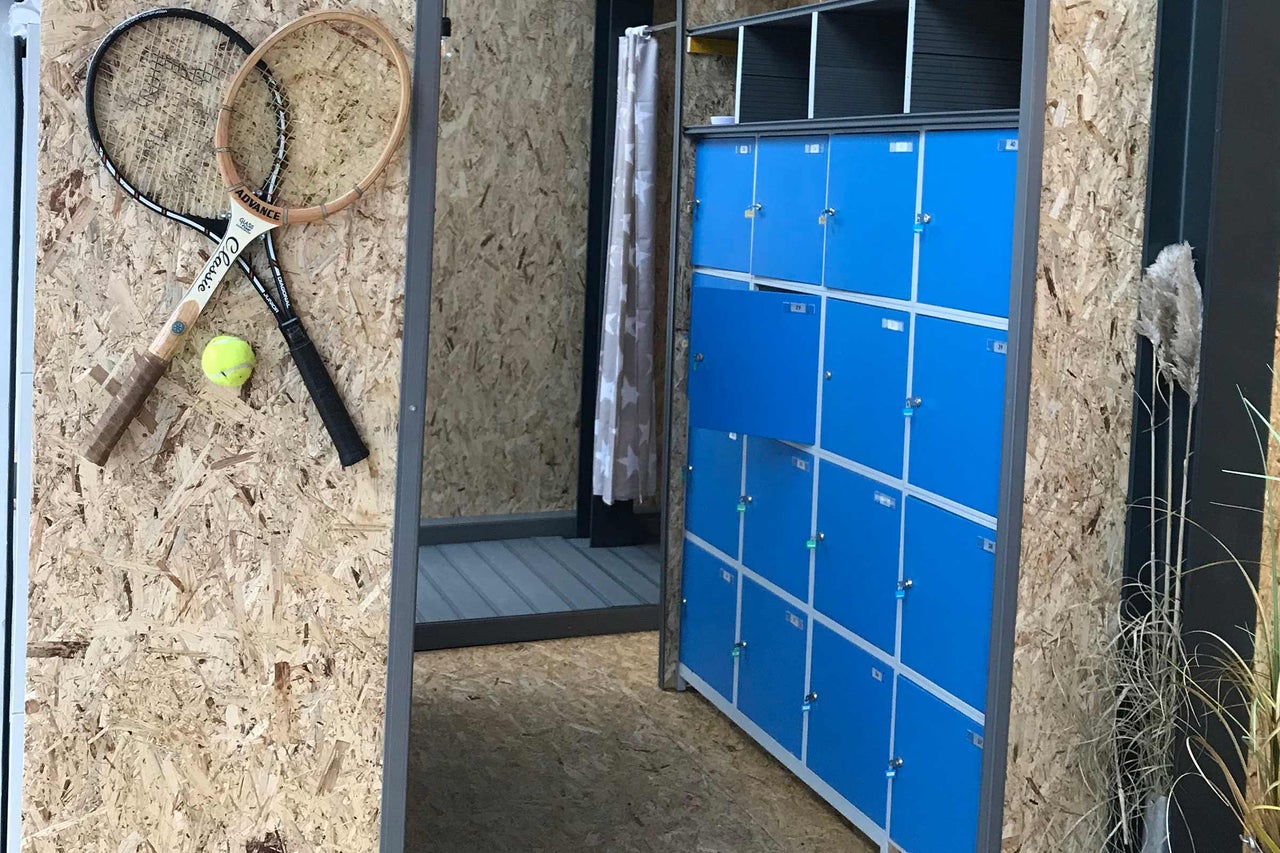 Innenraum mit blauen Schließfächern, Umkleidekabine mit Vorhang, zwei Tennisschlägern und einem Tennisball