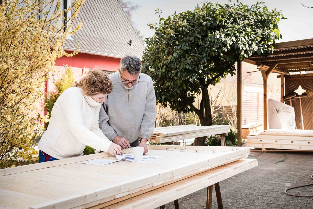 Zwei Personen betrachten Baupläne auf einem Tisch mit Holz im Garten.