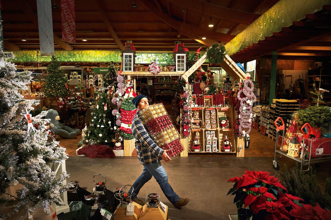 Mann trägt Christbaumkugeln im Hornbach Markt mit Weihnachtsdekoration.